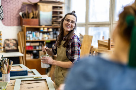 Portrait of smiling female artist holding paintbrush while working in art studioの写真素材