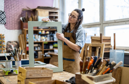 Portrait of a female carpenter working in her workshop. She is wearing glasses and holding a wooden frame.の写真素材