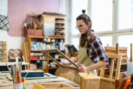 Young female artist working in her studio, she is wearing glasses and apronの写真素材