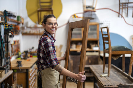 Portrait of smiling female craftsman standing by wooden frame in workshopの写真素材