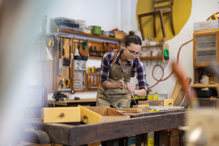 Female carpenter working in her workshop, she is wearing glasses and apronの写真素材