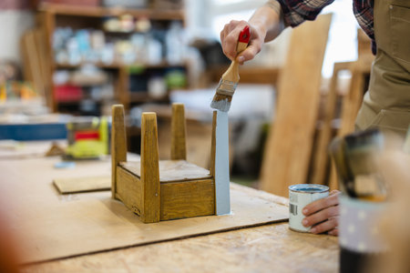 Carpenter using paintbrush to paint wooden chair in his workshopの写真素材