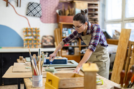 Confident female artist working on her craft in her workshop. She is wearing glasses and a plaid shirt.の写真素材