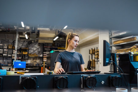 Portrait of young woman working on computer in production line at factoryの写真素材