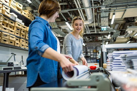 Two young female workers working together on a printing machine in a factoryの写真素材