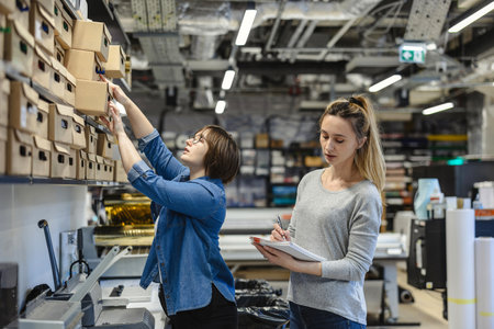 Young female worker and her colleague working together in warehouse, checking boxes. This is a freight transportation and distribution warehouseの写真素材