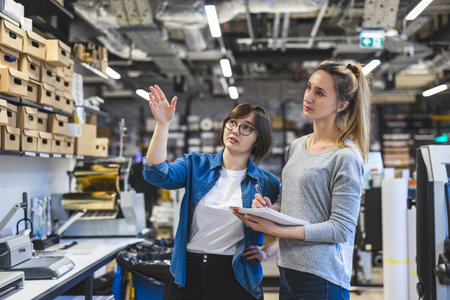Portrait of two young female engineers discussing over blueprint at workbench in workshopの写真素材