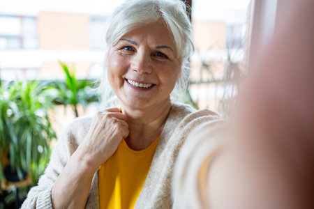 Portrait of smiling senior woman taking selfie with mobile phone at homeの写真素材