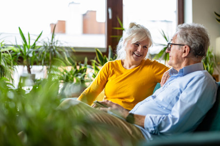 Senior couple sitting on sofa and looking at each other in living roomの写真素材