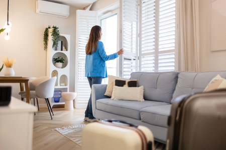 Young woman standing in living room, looking at windowの写真素材