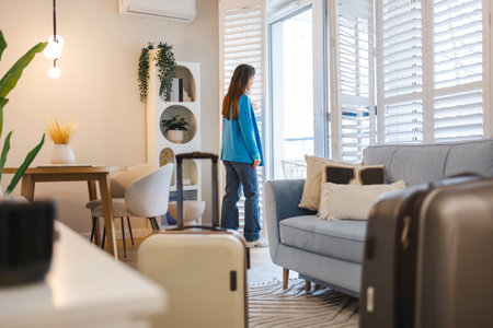 Rear view of young woman with a suitcase in modern living roomの写真素材