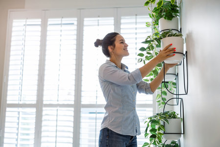 Portrait of young woman with plant in pot standing in living room at homeの写真素材