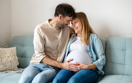 Pregnant couple sitting on sofa in living room at home.の写真素材