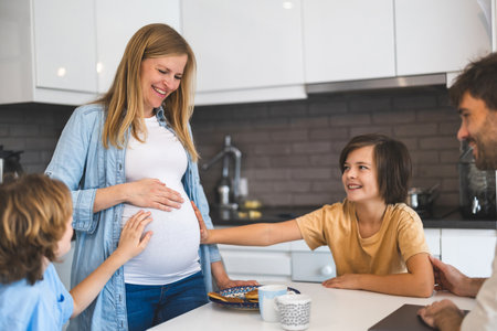 Smiling pregnant woman touching her belly with hands in kitchen at homeの写真素材