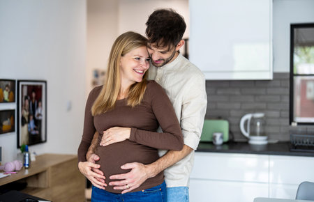 Happy pregnant couple embracing each other in kitchen at home. Focus on pregnant womanの写真素材