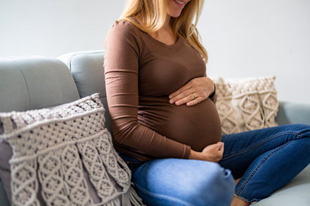 Midsection of pregnant woman sitting on sofa in living room at homeの写真素材