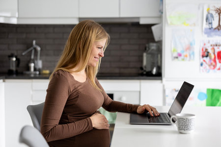 Pregnant woman using laptop in the kitchen at home. Maternity prenatal care and woman pregnancy concept.の写真素材