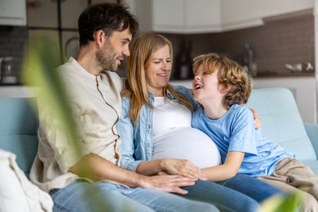 Happy pregnant woman with her husband and son in living room at homeの写真素材