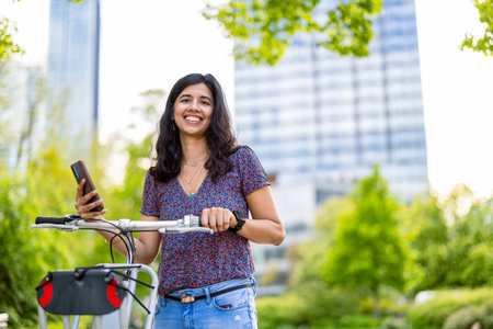 Portrait of happy young woman using mobile phone while standing with bicycle in cityの写真素材