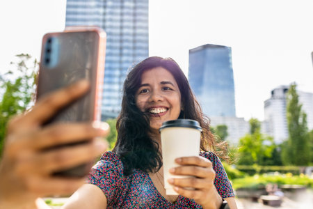 Beautiful latin woman taking a selfie in the city with coffeeの写真素材