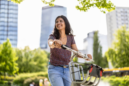 Beautiful Indian woman riding a bicycle in the city on a sunny dayの写真素材