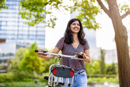 Portrait of a happy young woman with bicycle in the city parkの写真素材
