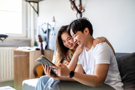 Happy asian couple using tablet in living room at home. Lifestyle and leisure concept.の写真素材