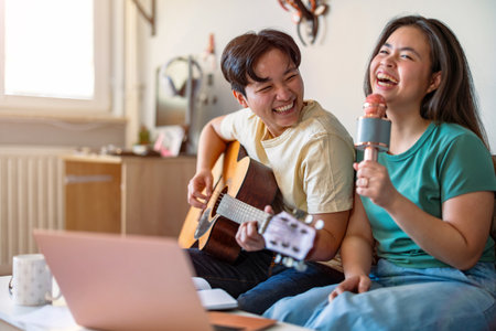 Young asian couple playing guitar and singing together with laptop at homeの写真素材