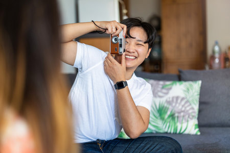 Happy asian man taking a picture of his girlfriend at home.の写真素材