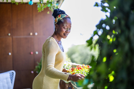Portrait of smiling african american woman cutting flowers on terrace at homeの写真素材