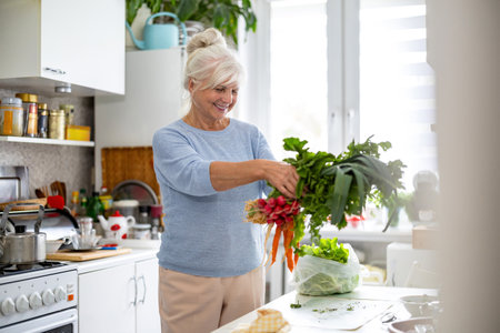 Portrait of smiling senior woman preparing vegetable salad in kitchen at homeの写真素材