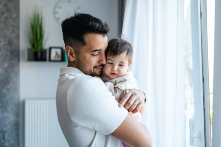 happy father holding baby daughter in arms at homeの写真素材
