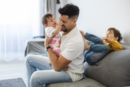 Happy young father playing with his two little daughters while sitting on sofa at homeの写真素材