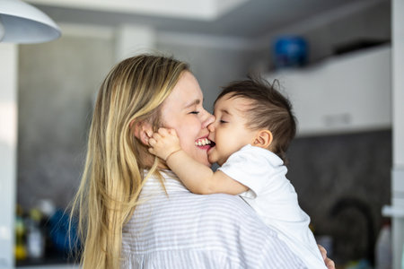 Portrait of a mother kissing her daughter in the kitchen at homeの写真素材