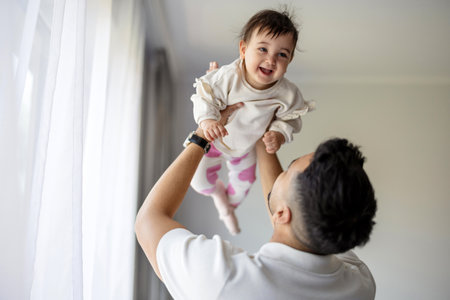 Happy father playing with his baby daughter in the room at home.