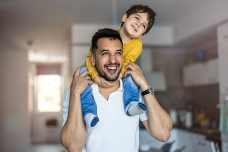 Portrait of father carrying his son on shoulders in kitchen at home