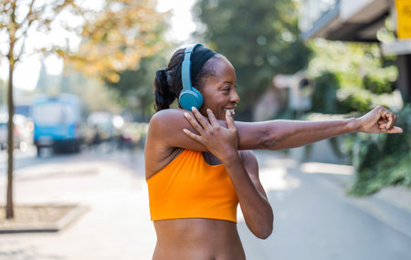 Side view of happy young woman listening to music with headphones while exercising in cityの写真素材