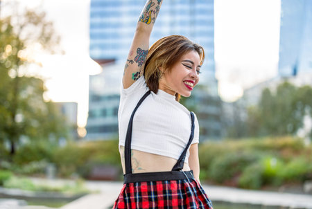 A young hipster girl with tattoos on her arms, wearing a plaid skirt, posing in an urban contextの写真素材
