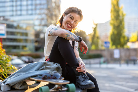 Portrait of smiling young woman sitting with a skateboard in the cityの写真素材