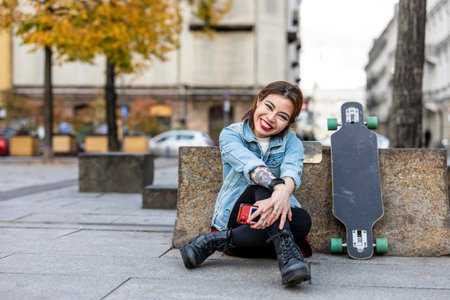 Beautiful young woman sitting on a skateboard in the city.の写真素材