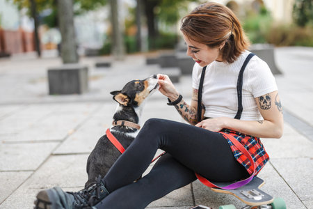 Beautiful girl with tattoos on her arms sitting on the pavement with her dogの写真素材