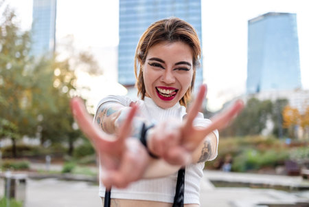 Portrait of a beautiful young woman with tattooed arm showing victory signの写真素材