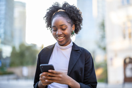 Portrait of smiling african american woman using mobile phone in cityの写真素材