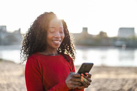 Portrait of a smiling young woman using mobile phone on the beachの写真素材