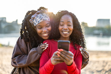 Two african american women using mobile phone together on the beachの写真素材