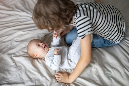 Boy playing with his baby brother on the bed at homeの写真素材