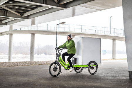 Young man riding an electric bicycle under the bridge in winter.の写真素材