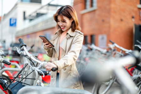 Young woman using mobile phone while standing with bicycle in the city.の写真素材