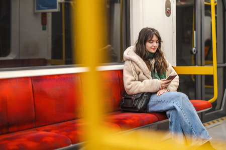 Young woman sitting on the bench and using mobile phone in the subwayの写真素材