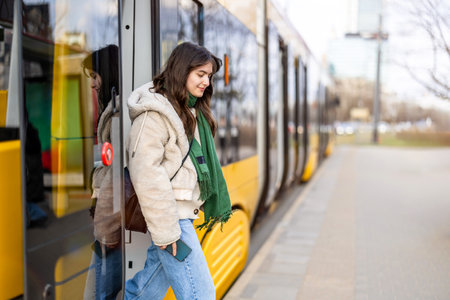 Portrait of a young brunette woman with long hair in a white jacket and jeans on the background of a yellow tramの写真素材